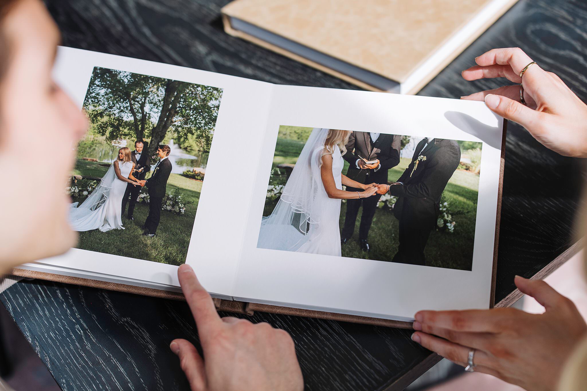 A couple turning a page in a designed album together, both hands on the book, engagement ring catching the light