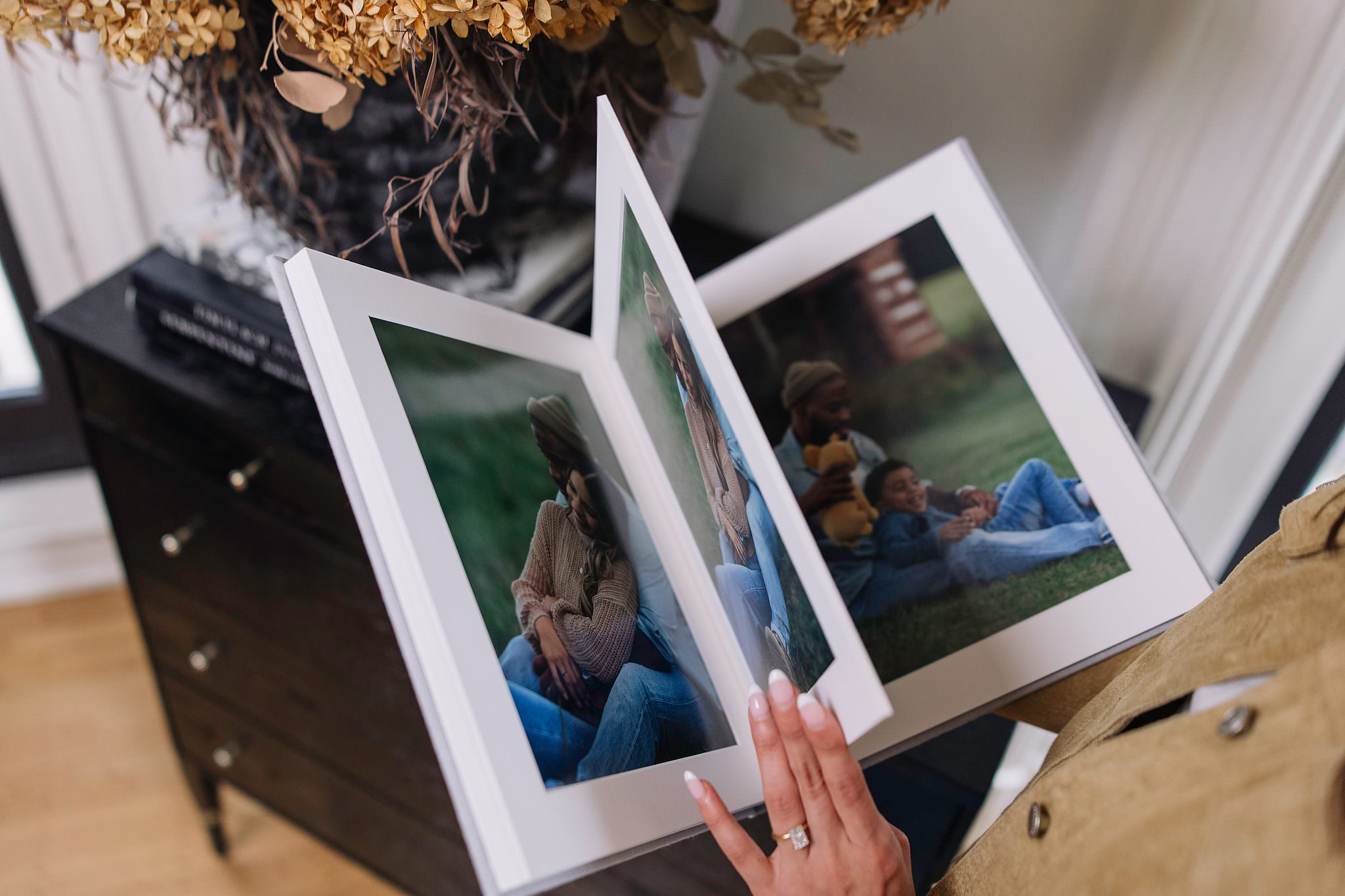 A matted folio album lifted open to a tender family portrait spread, dried hydrangeas in the foreground