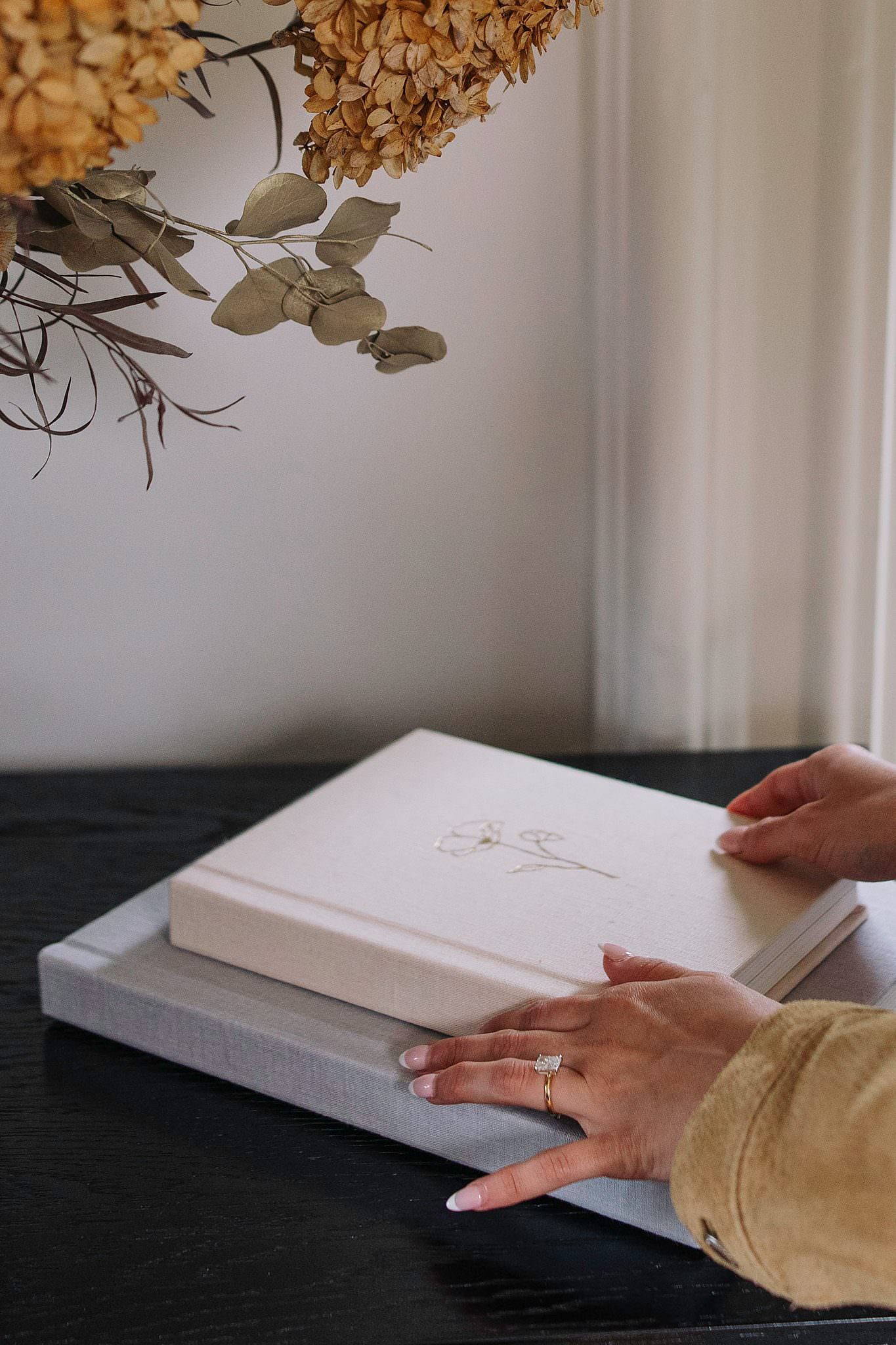 A linen folio album resting on top of a presentation box with dried hydrangea above