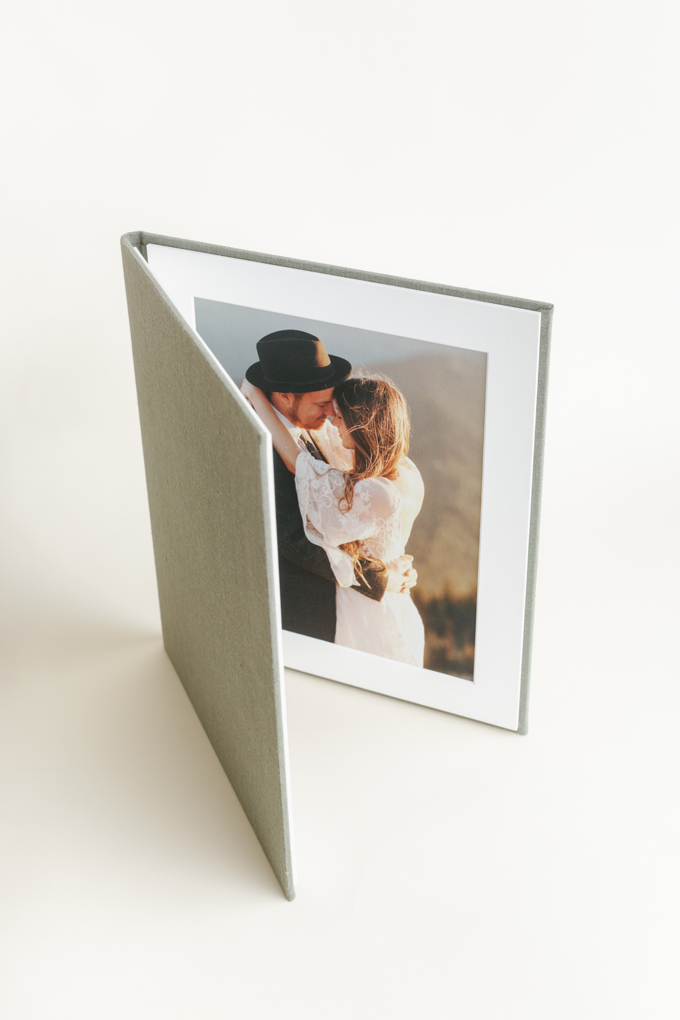 A grey linen bi-fold matted folio standing open to show a wedding portrait inside